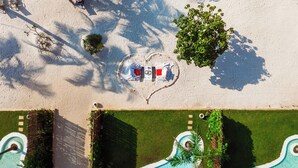 Eine Luftaufnahme eines Resorts mit Poolbereich, einer herzförmigen Anordnung von Liegestühlen und einem kleinen Baum.
