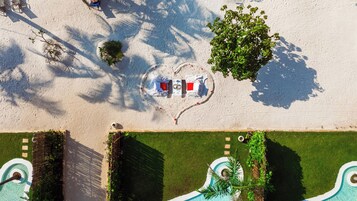 Vista aérea de un complejo turístico con zona de piscina, una disposición de sillas con forma de corazón y un pequeño árbol.