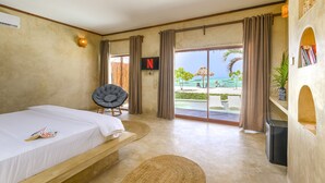 Ein Schlafzimmer mit Bett, Sessel, Fernseher und Blick auf Pool und Strand.