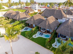 Een resort met villa's met rieten daken, een zwembad en een strand.