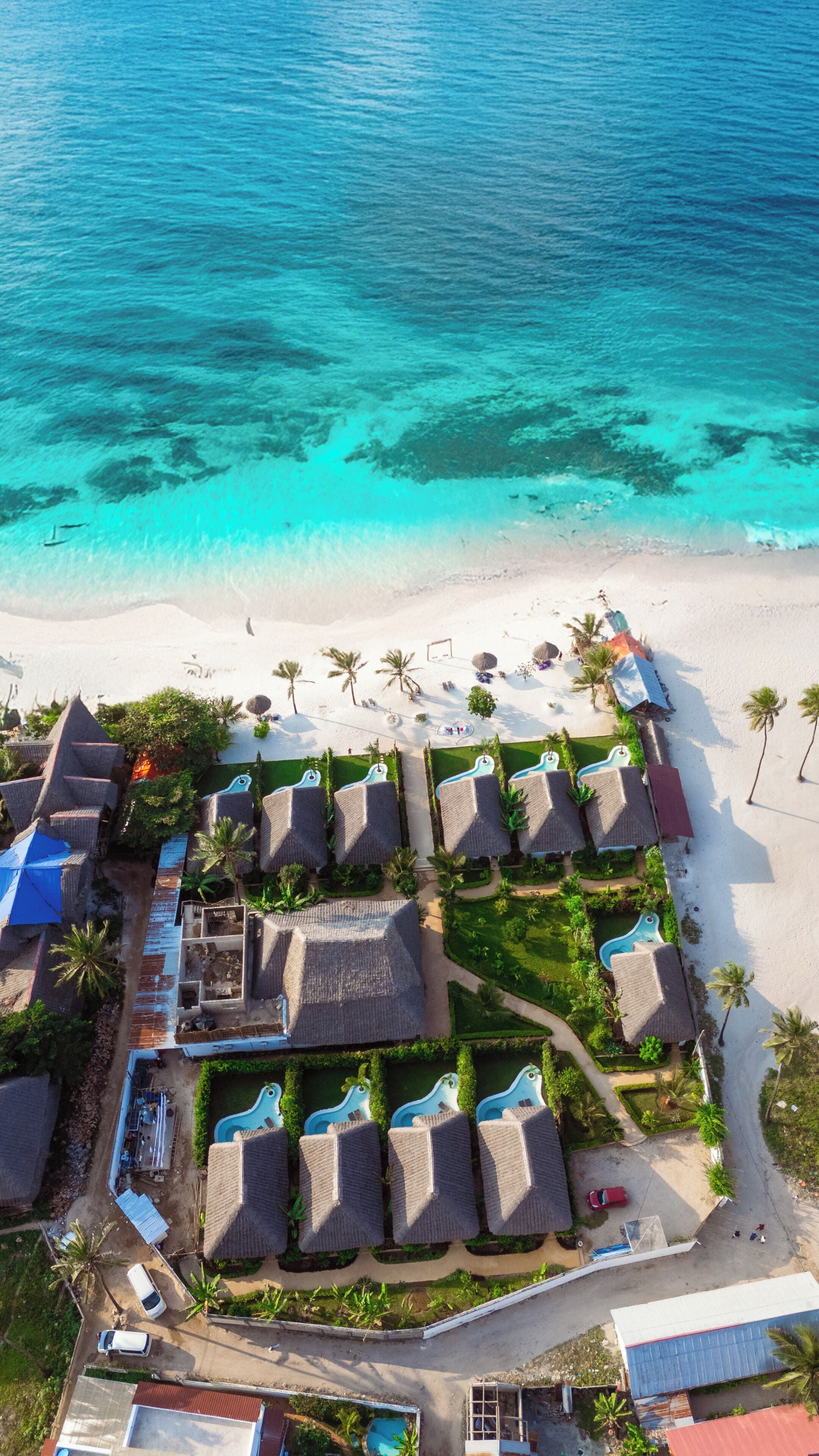 Vue aérienne d’un complexe hôtelier comprenant plusieurs hébergements de type bungalow, une piscine et une plage.