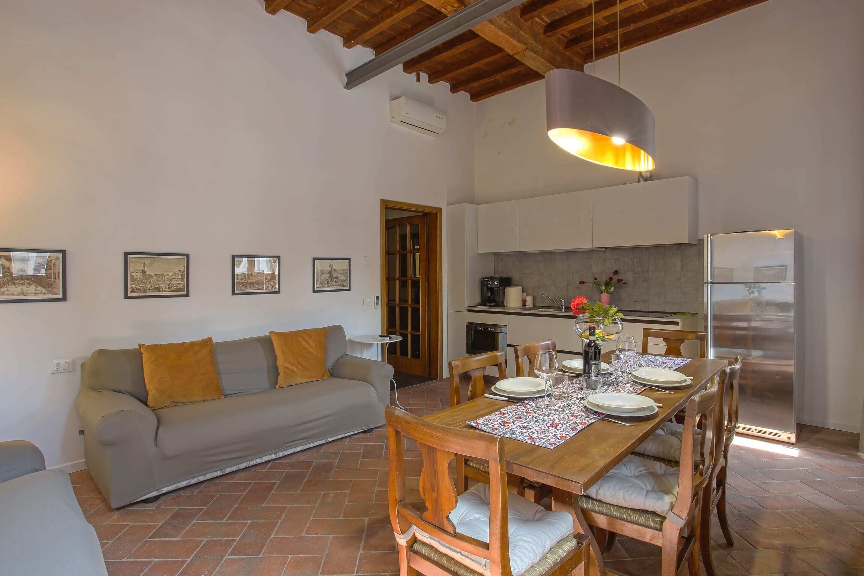 A dining area with a wooden table set for four, a sofa, and a kitchen in the background.