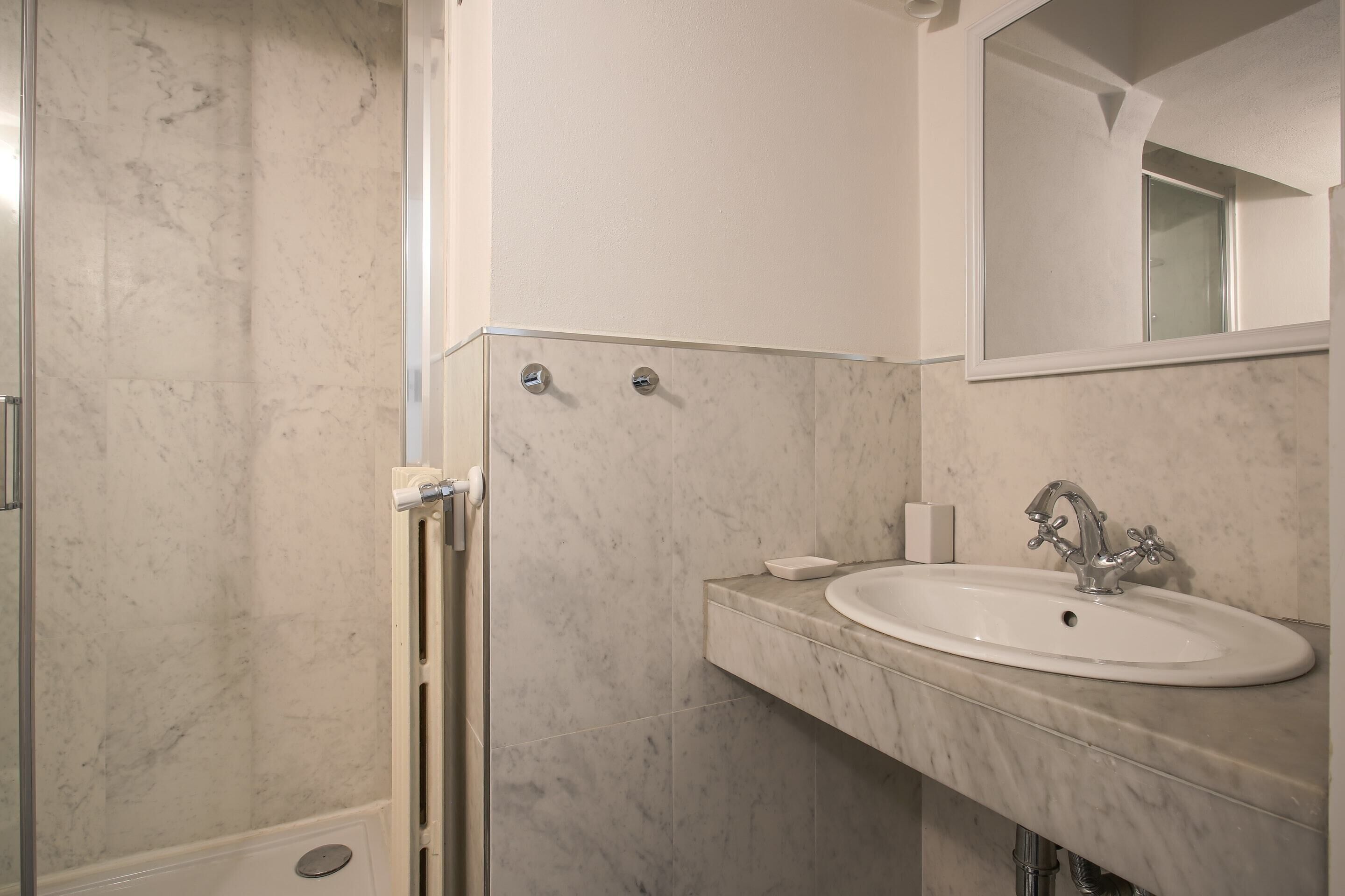 A bathroom with a marble sink, a mirror, and a shower area.