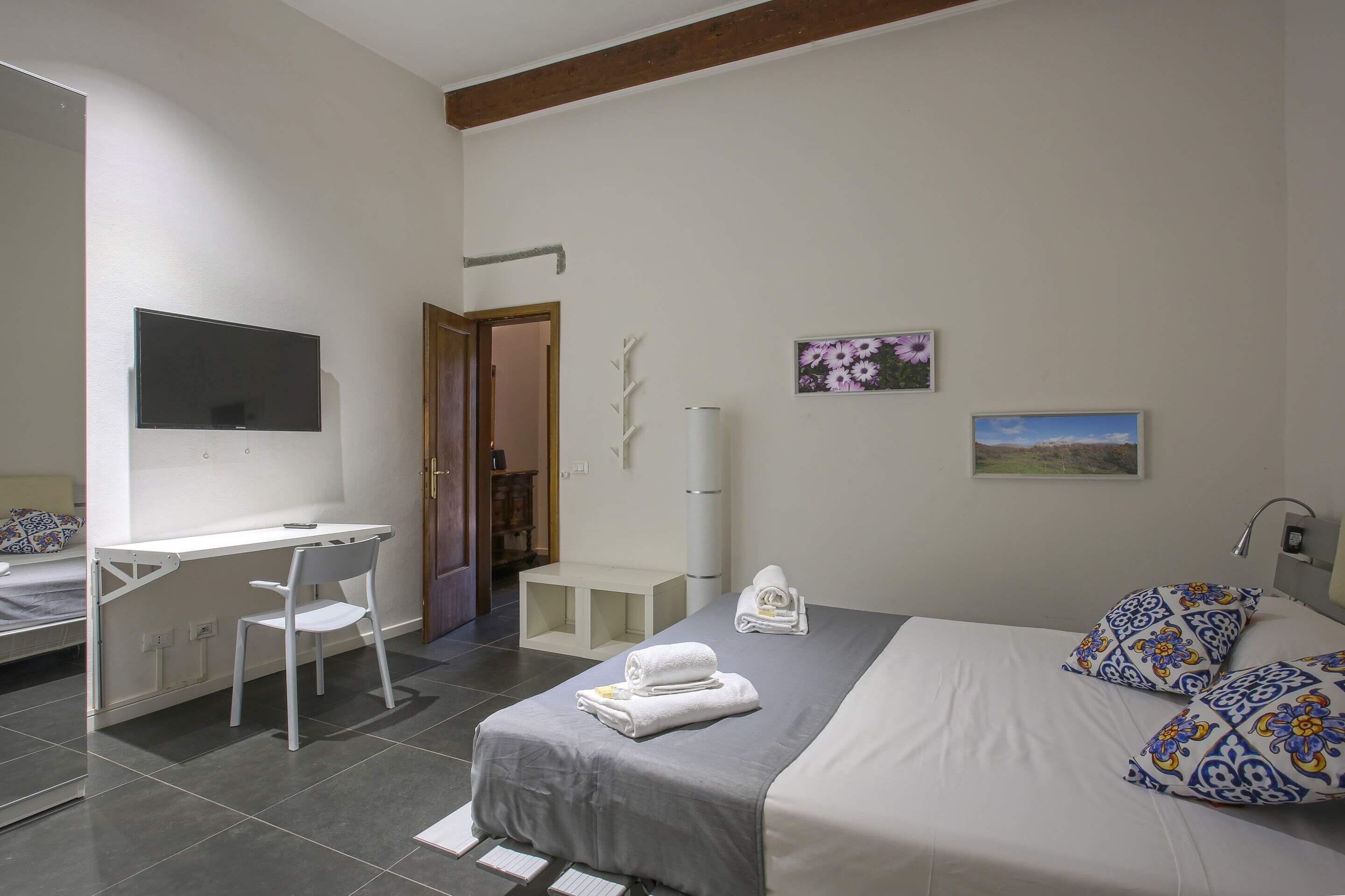 A bedroom with a bed, a desk, a chair, a TV, and a bathroom door.