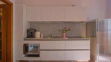 A modern kitchen with white cabinets, a built-in oven, a coffee maker, and a potted plant.