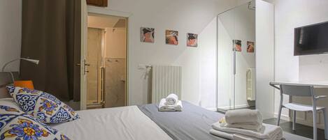 A hotel room with a bed, a desk, a chair, a TV, and artwork on the wall.