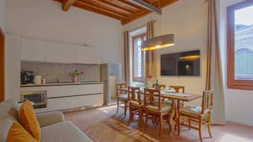 A modern kitchen with white cabinets, a dining area with wooden chairs, and a large window with curtains.