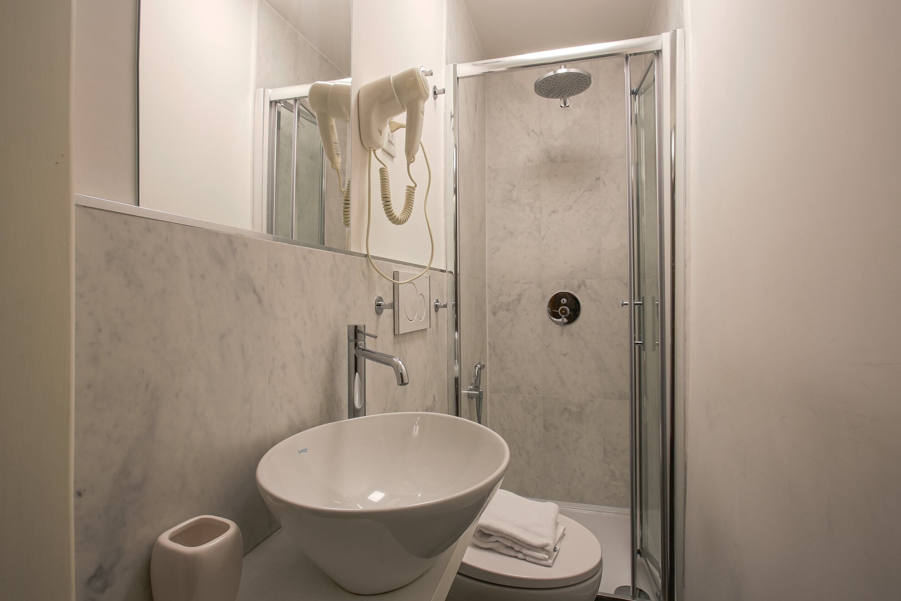 Een moderne badkamer met een groot wit wastafel, een toilet en een douche met glazen wanden.