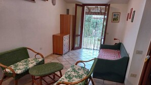 A room with two wicker chairs with floral cushions, a wooden cabinet, a green sofa, and a tiled floor. - PEPE house, cottage with garden 5 min from Campus beach, Villasimius  (Sardegna)