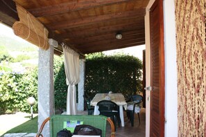 An outdoor patio with a table and chairs, a wicker chair, and a door leading to a covered area. - PEPE house, cottage with garden 5 min from Campus beach, Villasimius  (Sardegna)