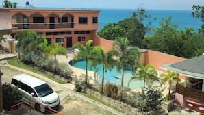 Un hotel con piscina, una camioneta blanca y vista al océano.