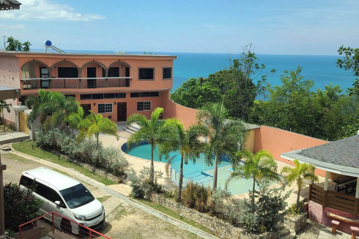 A hotel with a pool, a white van, and a view of the ocean.