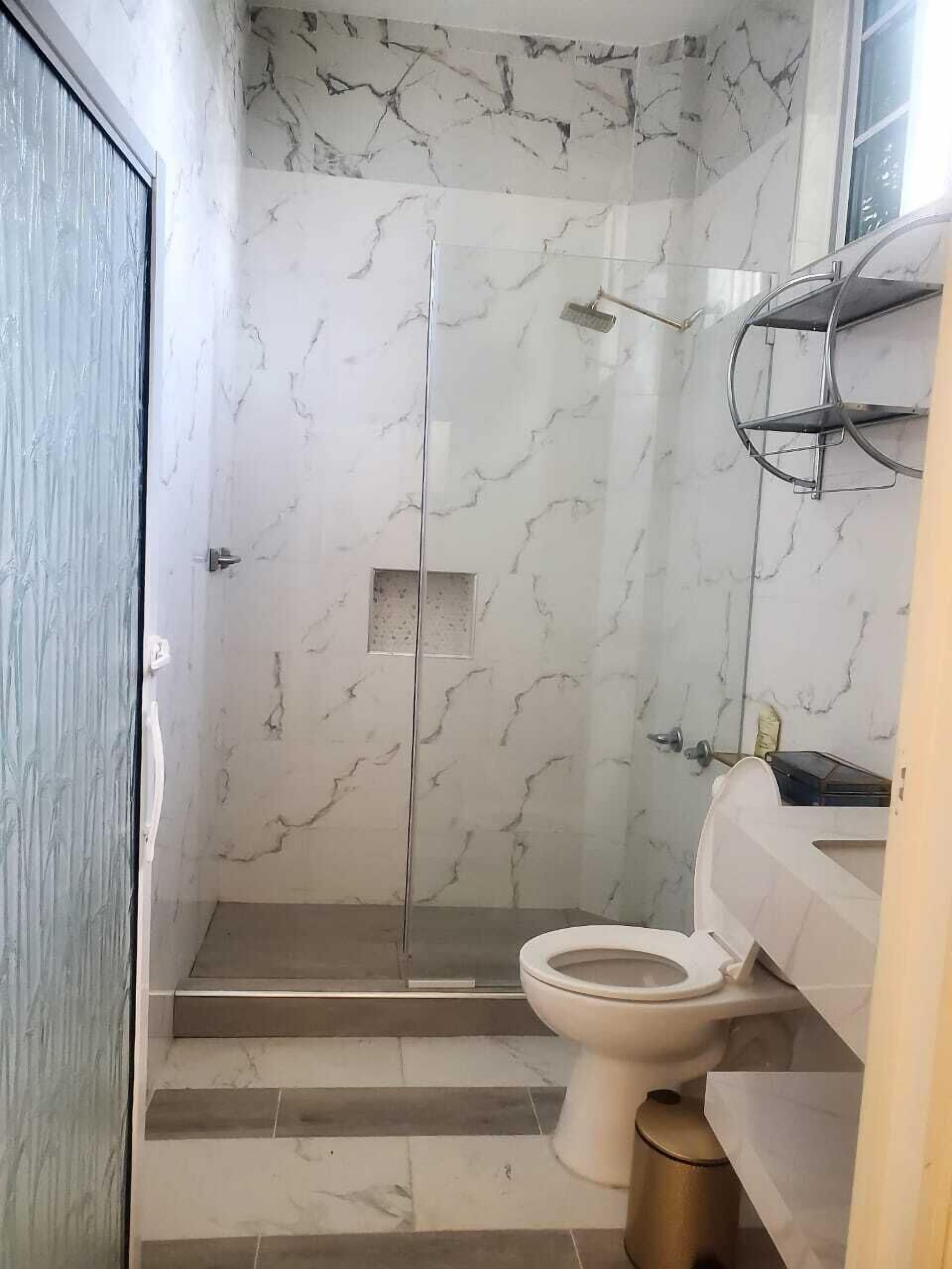 A bathroom with a glass shower enclosure, a toilet, and a sink with a towel rack.