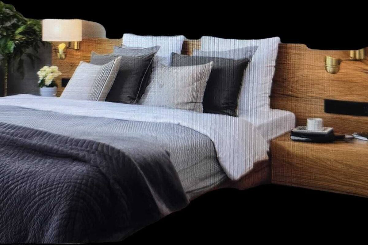 A modern bedroom with a large bed, a nightstand, a lamp, and a potted plant.