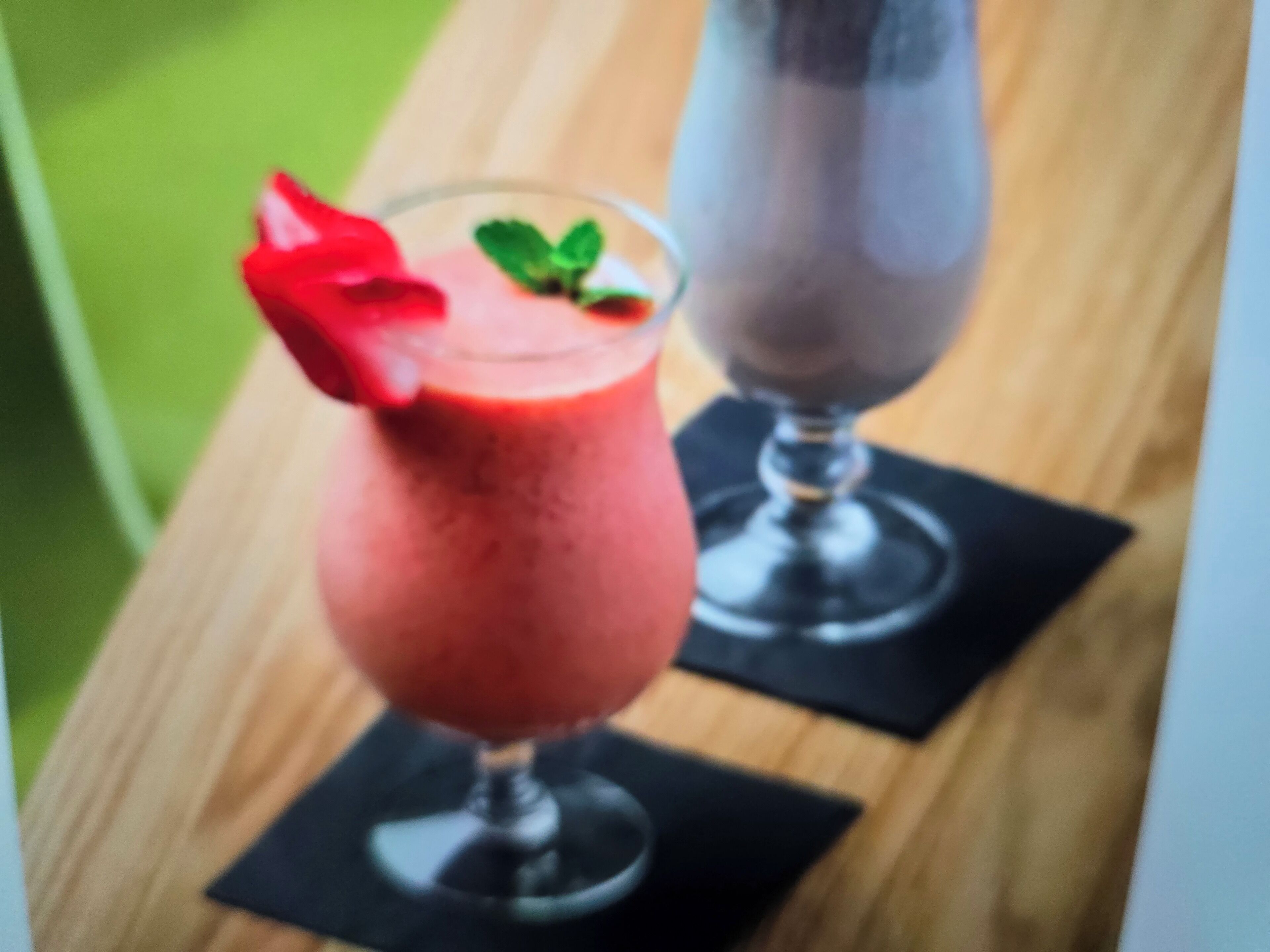 Two drinks on a wooden table with black coasters.
