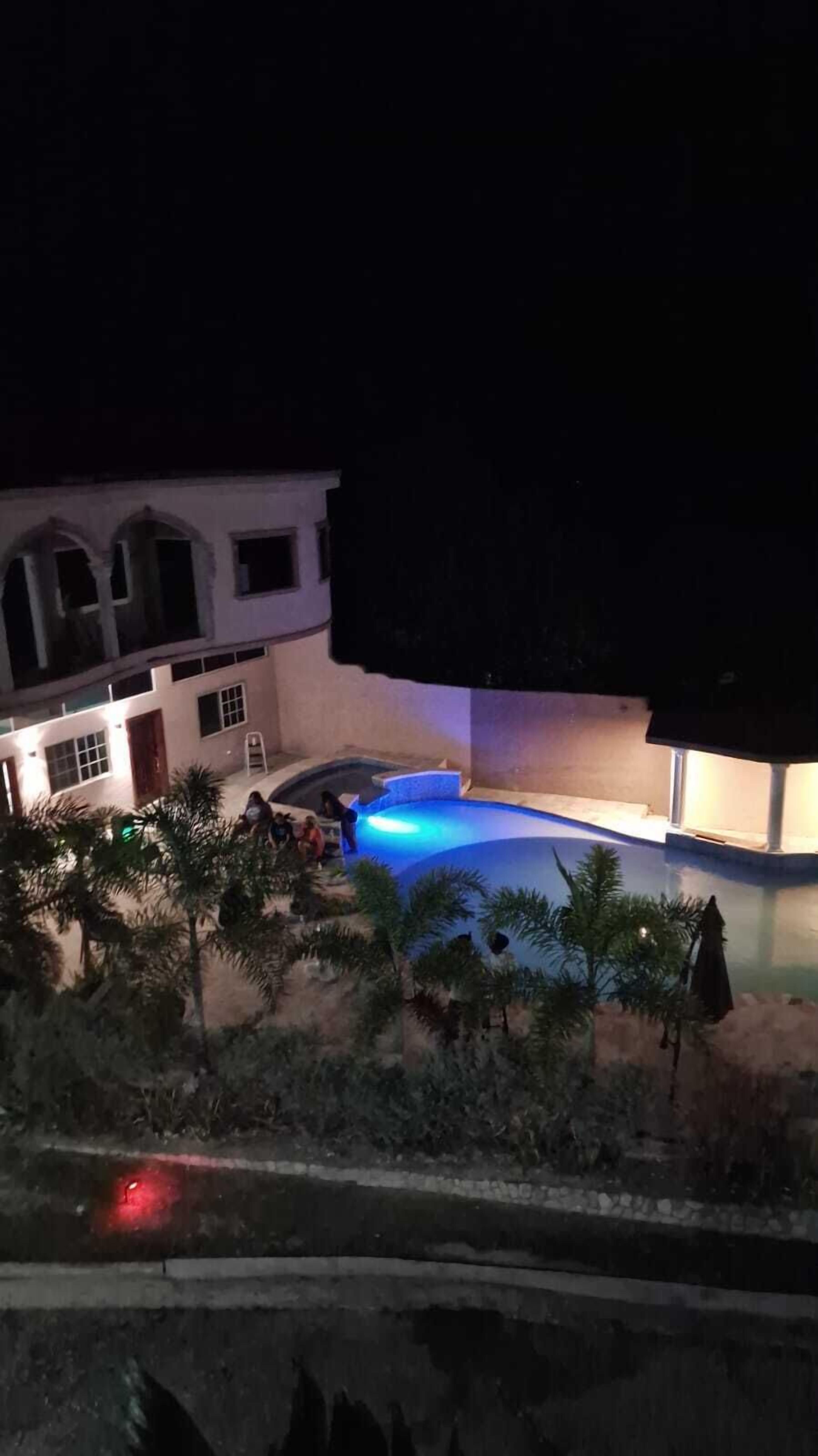 Un edificio residencial con piscina, rodeado de palmeras y un patio bien iluminado.
