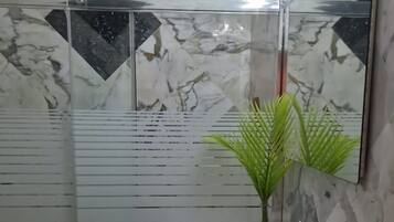 A bathroom with a glass shower enclosure, a marble backsplash, and a white sink with a towel and a plant.