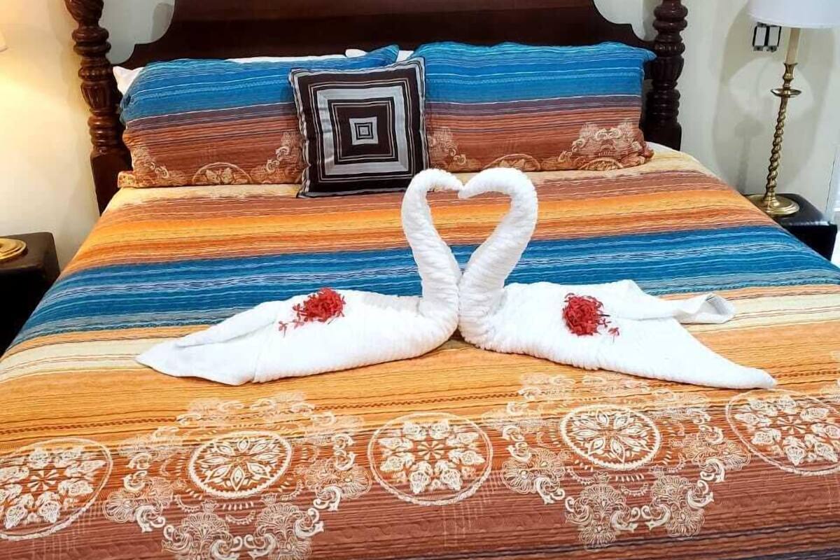 A bed with a striped bedspread, a heart-shaped towel arrangement, and a decorative pillow.