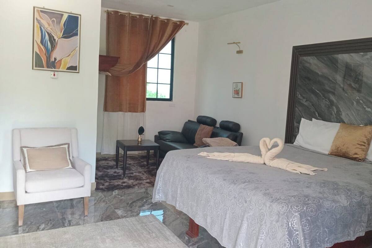 A hotel room with a large bed, a chair, a small table, and a window with curtains.