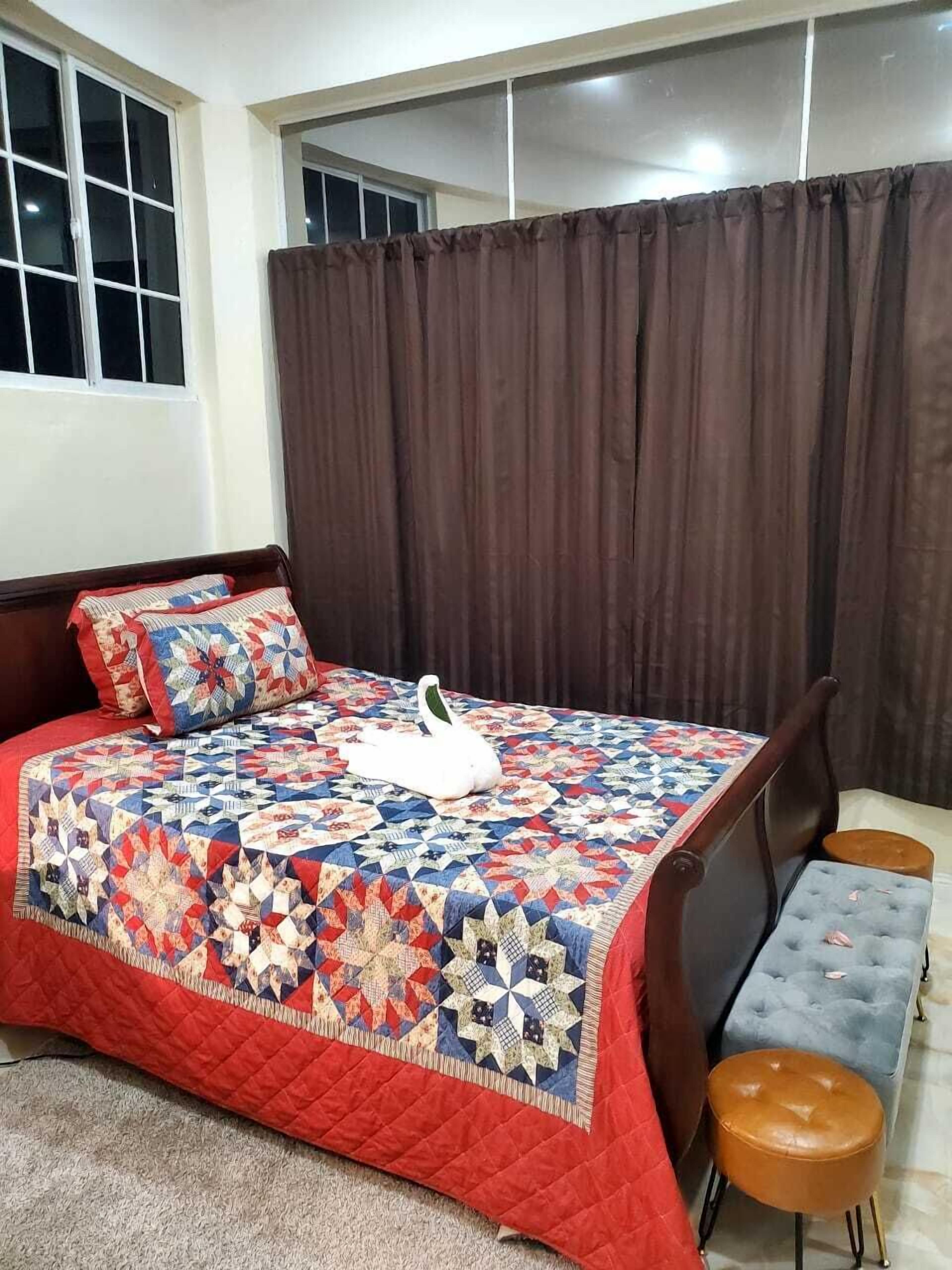 A bedroom with a large bed, a swan-shaped pillow, a quilt, a bench, and a window with curtains.