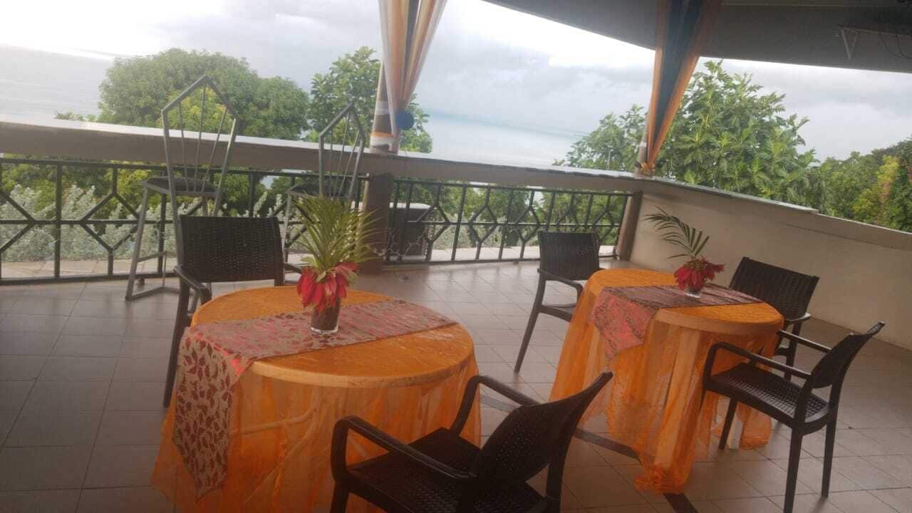 A terrace with round tables and chairs, some with tablecloths, and potted plants.