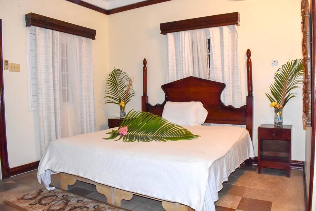 A neatly made bed with a white bedspread, flanked by two wooden nightstands with vases containing flowers.