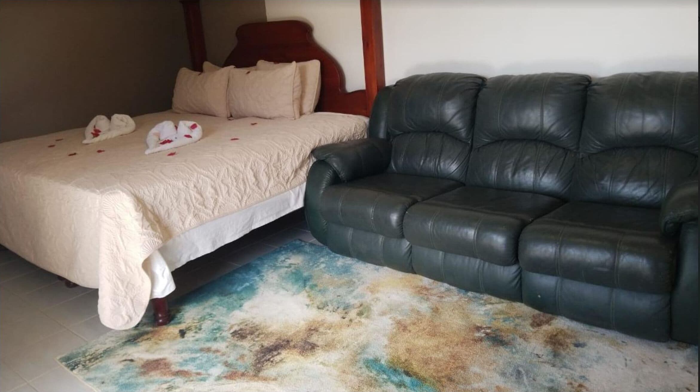 A bedroom with a bed, a black leather sofa, and a colorful rug.