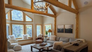 A spacious living room with large windows, a wooden ceiling, and a cozy seating area. - Quiet and Charming Big Sky home (Big Sky)