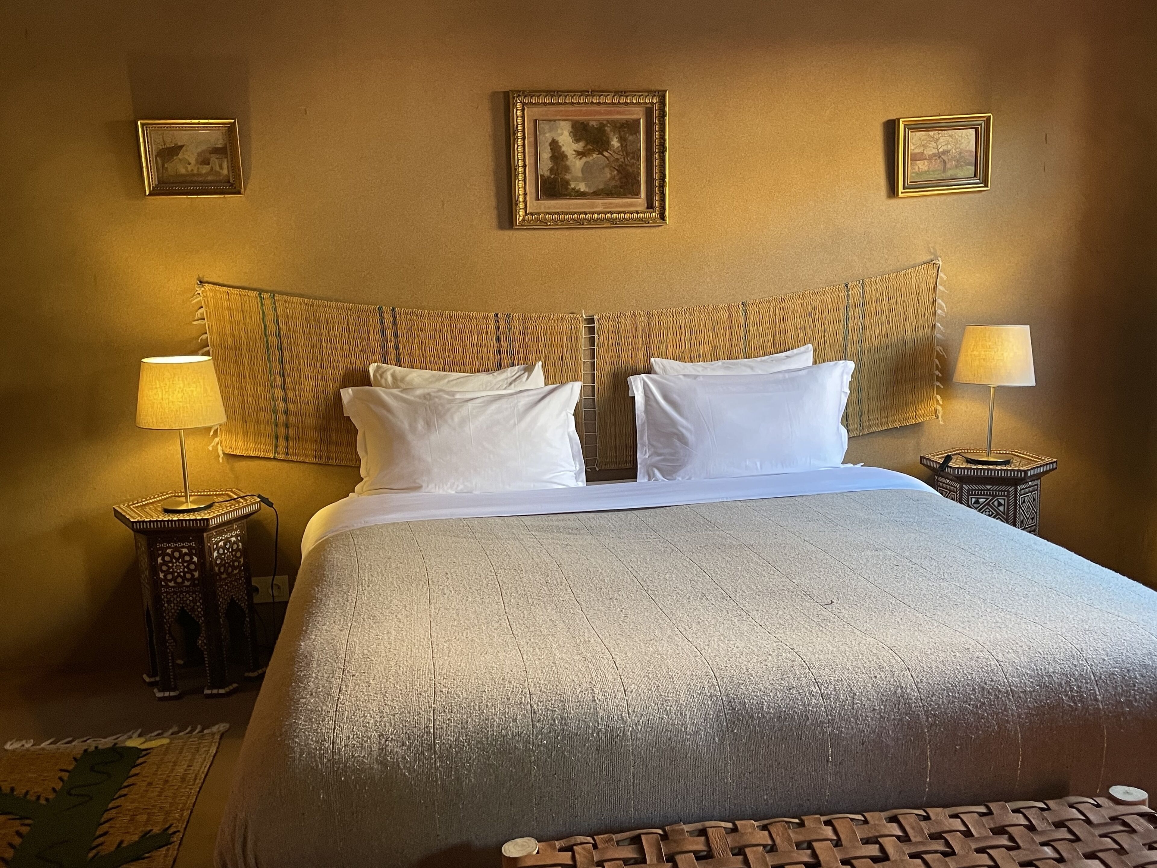 A neatly made bed with white linens, two bedside tables with lamps, and a woven headboard.