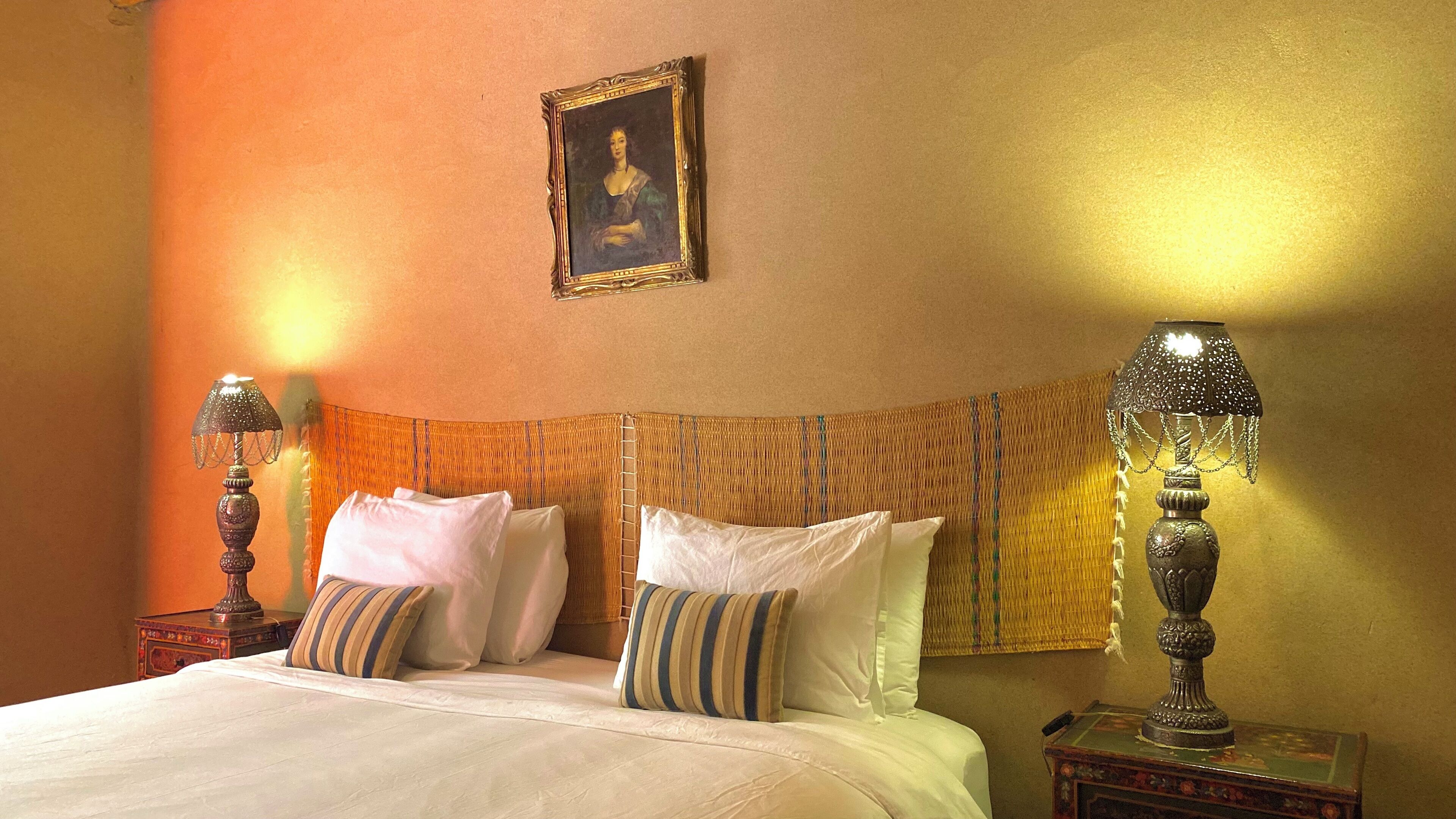 Una camera d'albergo con un letto, due abat-jour, un quadro appeso e una testiera in tessuto.