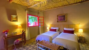 Une chambre d’hôtel avec deux lits, un bureau avec une lampe, une chaise et une petite table agrémentée d’objets décoratifs.