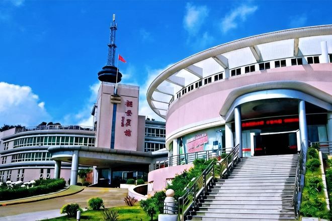 A modern building with a prominent tower, a curved entrance, and a staircase leading to the main entrance.