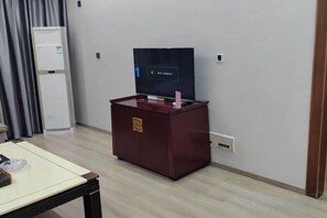 Habitación de hotel con televisión sobre un mueble bajo, una mesita y una puerta a la izquierda.