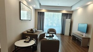 Una habitación de hotel moderna con sofá, sillón, mesa redonda y televisor de pantalla plana.
