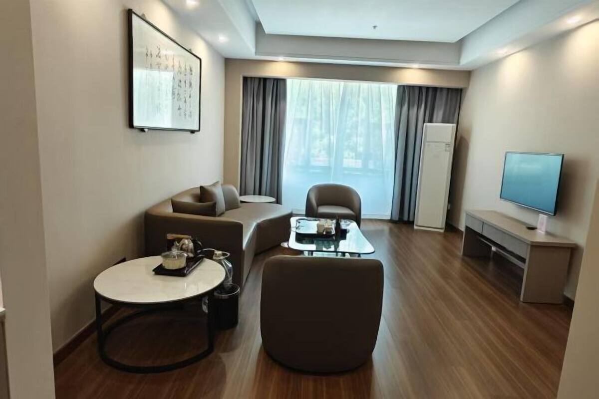A modern hotel room with a sofa, armchair, round table, and a flat-screen TV.