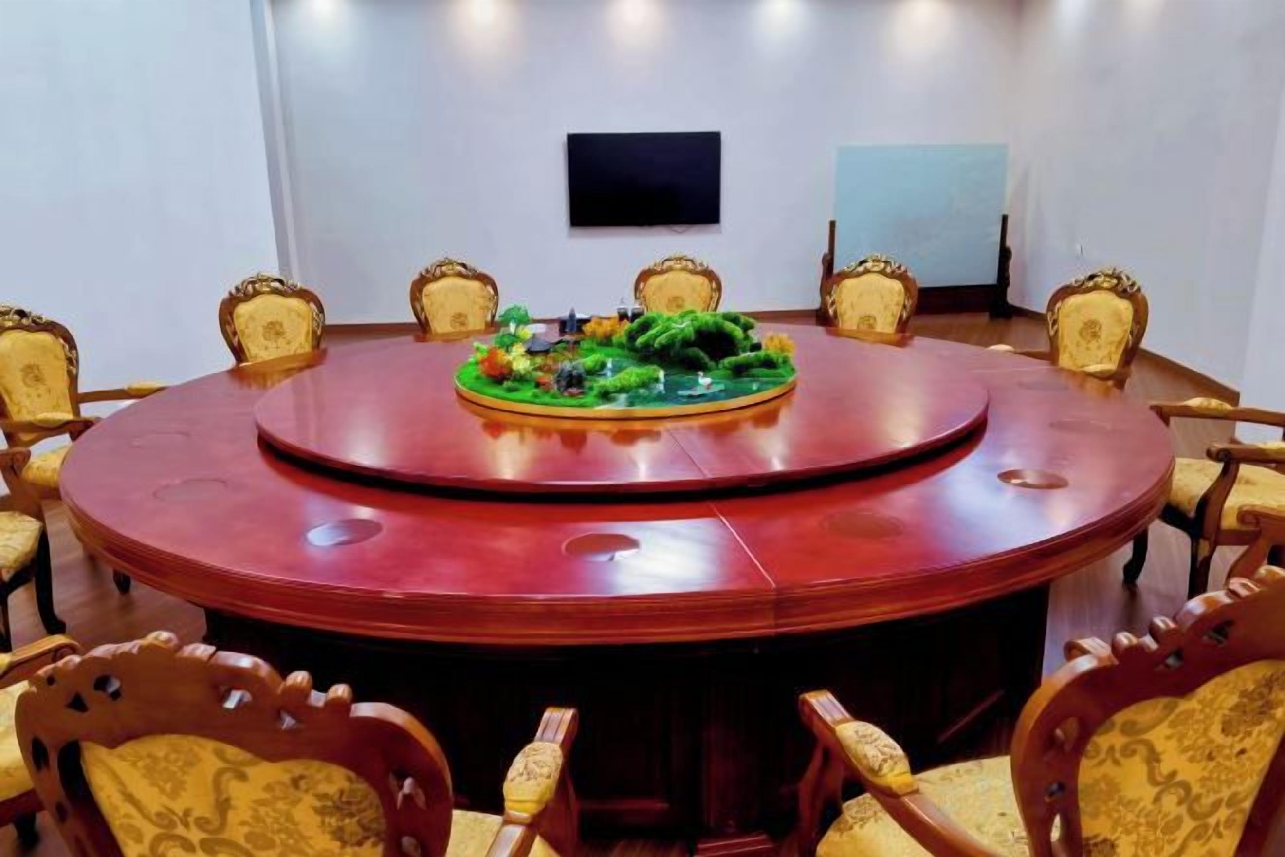 Un salón de conferencias con una mesa redonda, sillas y un televisor de pantalla plana en la pared.