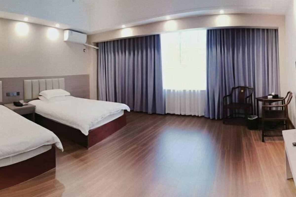 A hotel room with two beds, a desk, a chair, and a large window with curtains.