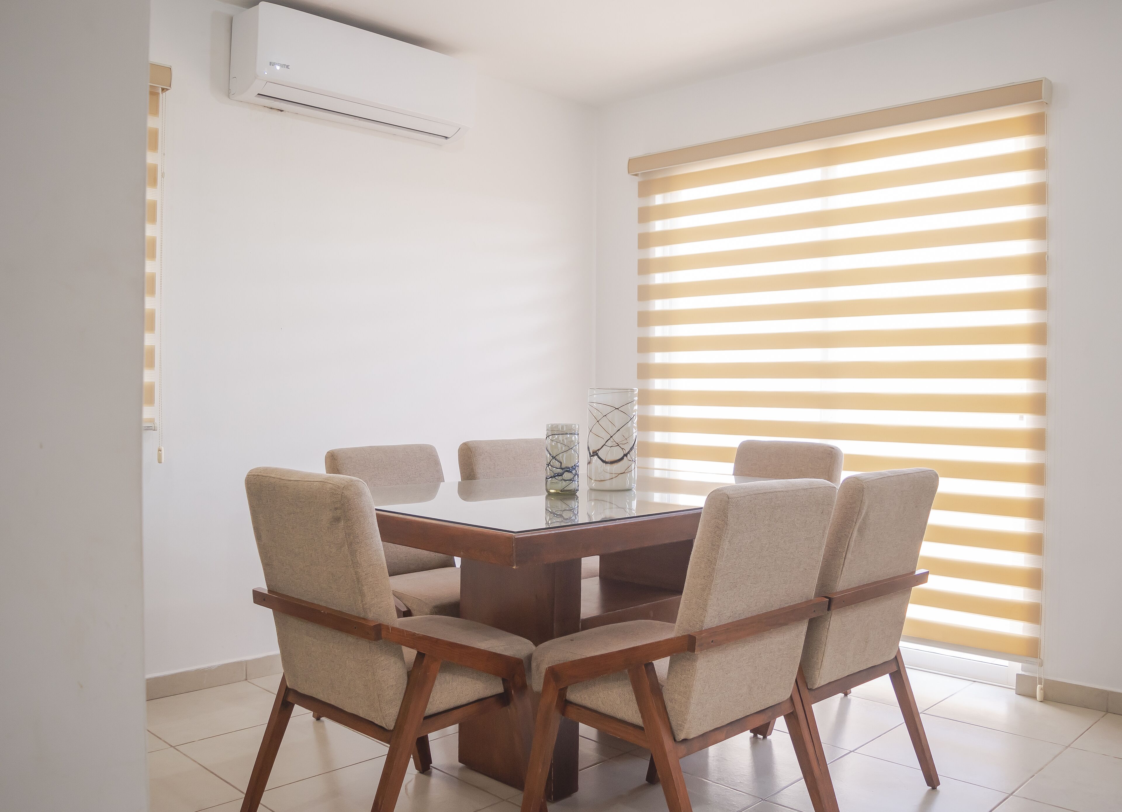 A dining area with a wooden table and four chairs, a glass vase, and a window with horizontal blinds.