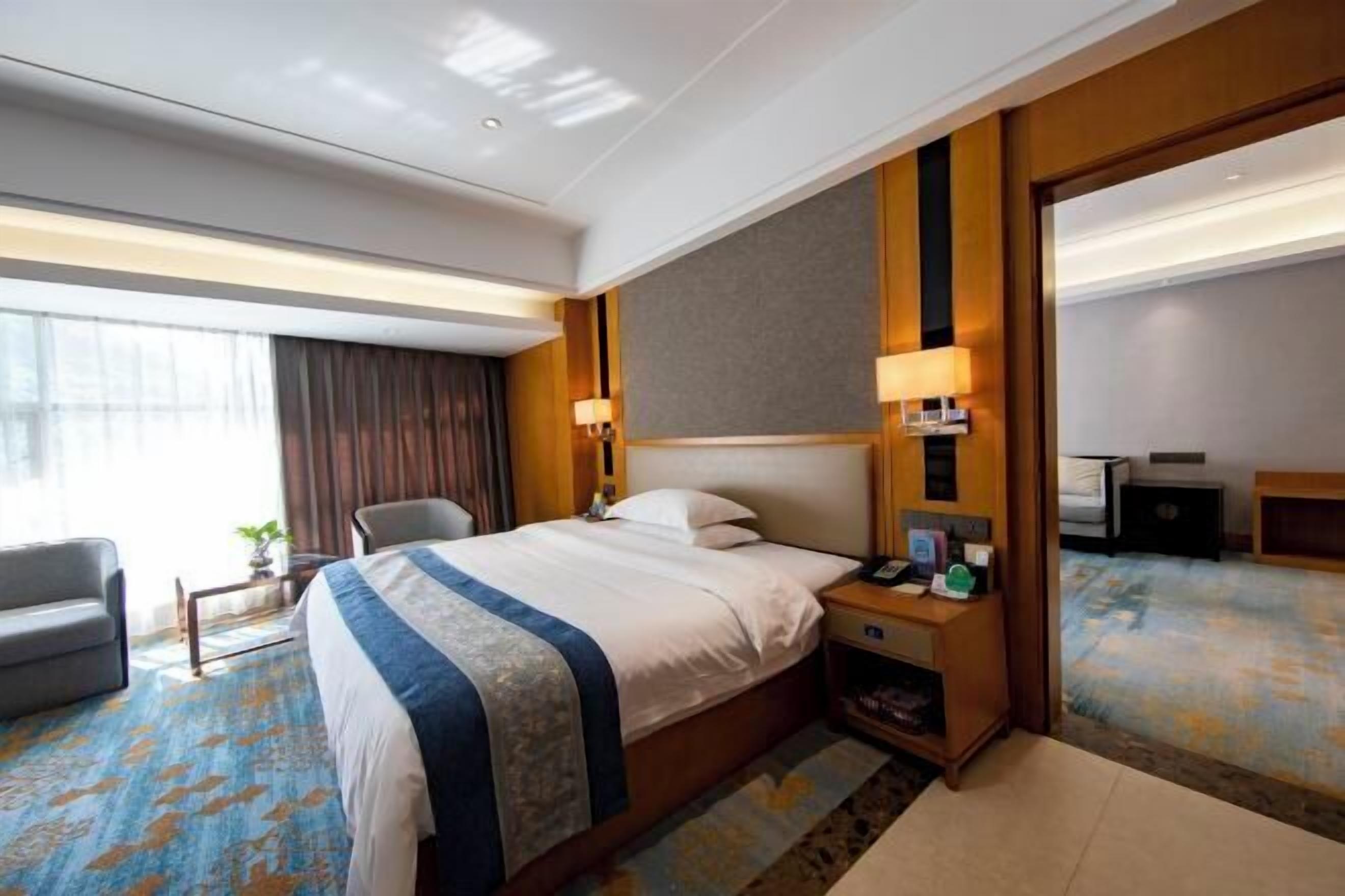 Habitación de hotel con cama, mesita de noche, lámpara, silla y un espejo grande.