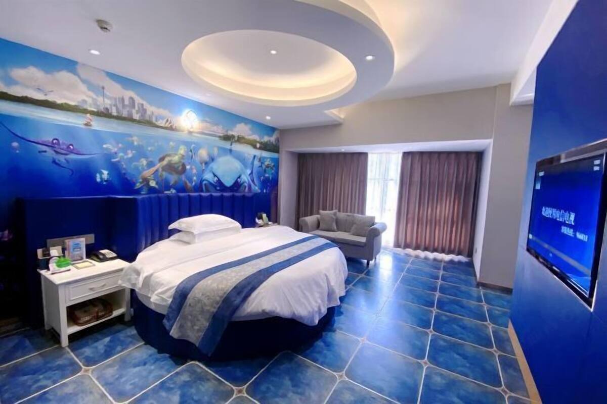 Ein Hotelzimmer mit einem großen Bett, einem Nachttisch, einem Fernseher und einem Wandgemälde.
