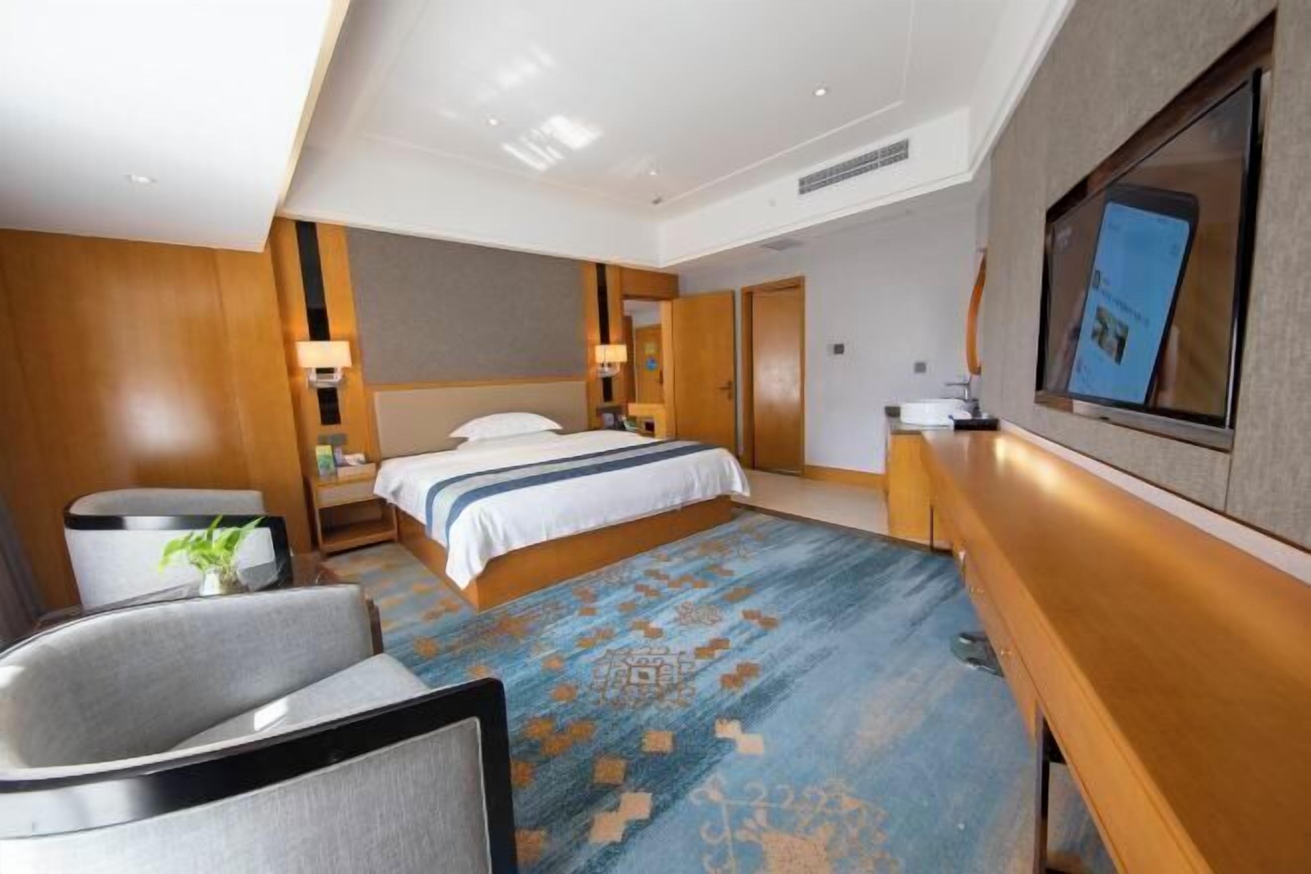 Ett modernt hotellrum med en stor säng, ett skrivbord, en stol och en tv som är monterad på väggen.