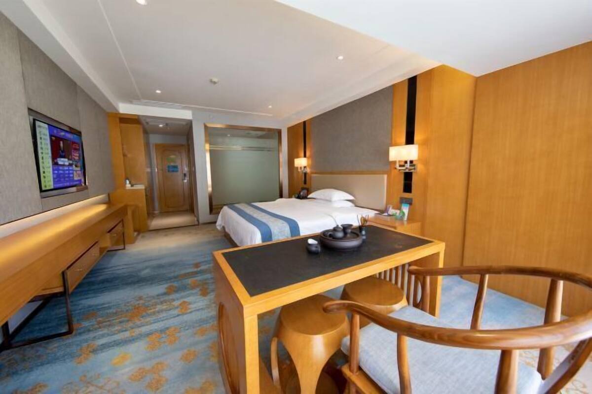 Ein Hotelzimmer mit Bett, Schreibtisch mit Stuhl, Fernseher und einem durch eine offene Tür einsehbarer Badezimmer.