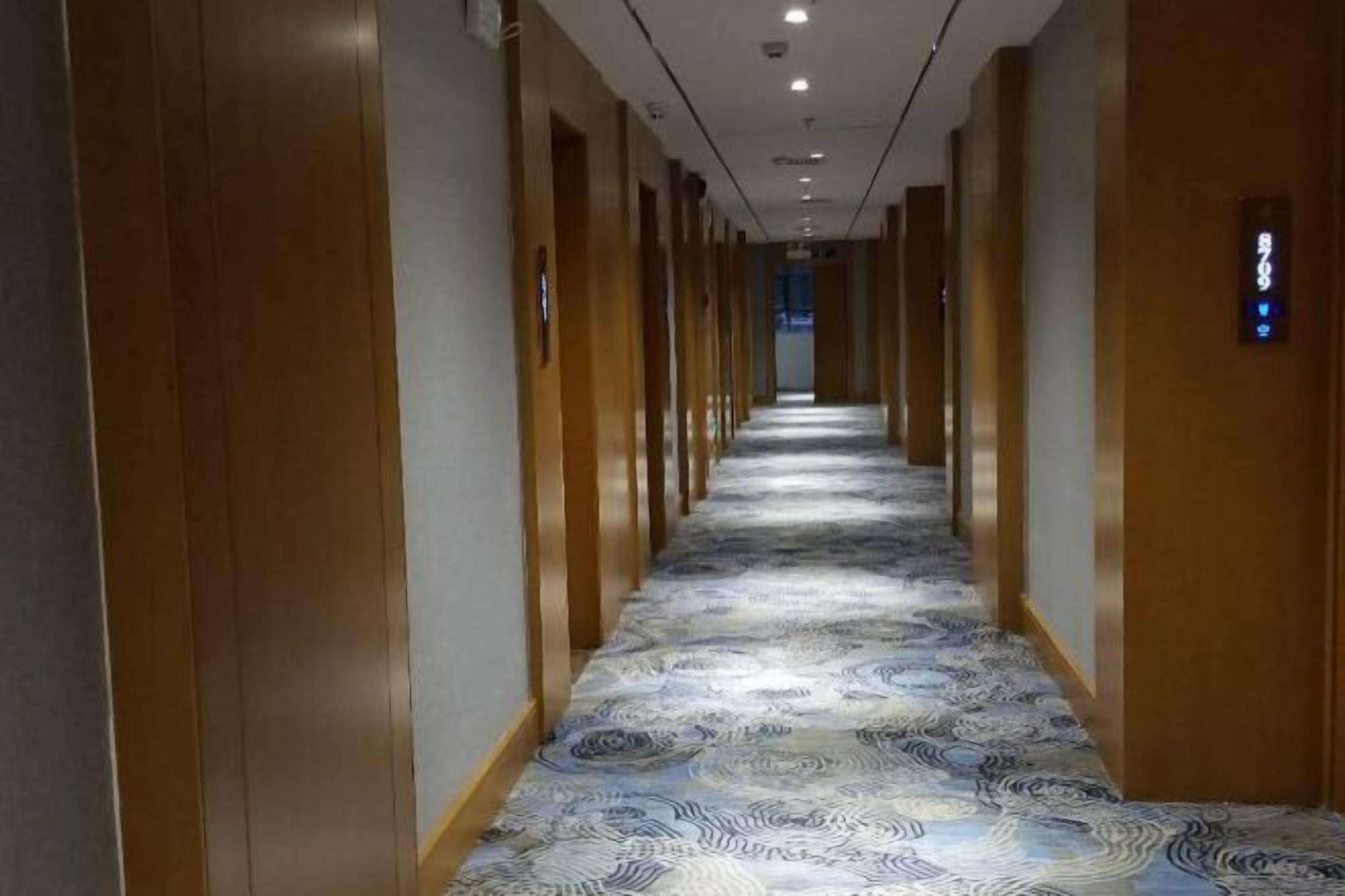 Een hotelgang met houten lambrisering, een kamergestreept tapijt en een bord met kamer nummers.