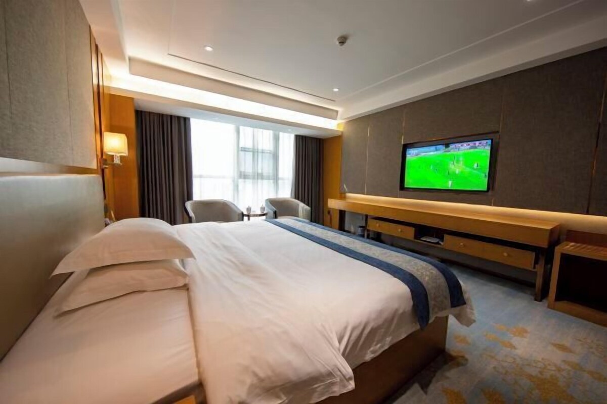 A hotel room with a large bed, a TV on the wall, a desk, and a chair.