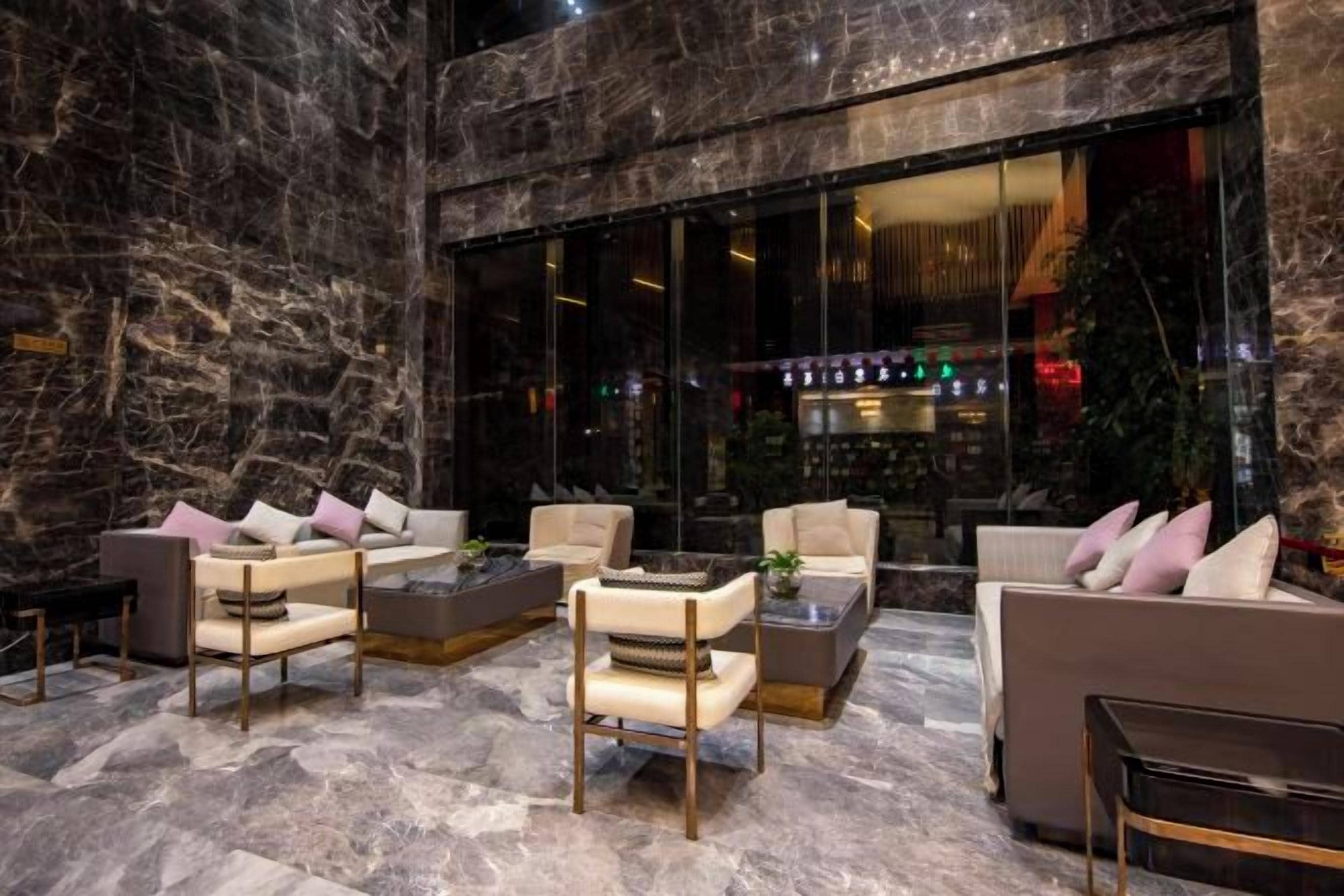 Um hall de entrada com piso de mármore, disposição de assentos e área de bar visíveis através do vidro.