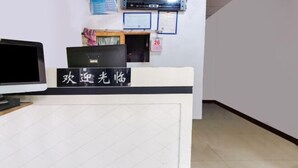 Un comptoir d’accueil avec une enseigne en caractères chinois, un écran d’ordinateur et un panneau d’affichage fixé au mur.
