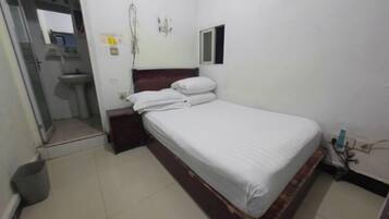 A small, clean room with a single bed, a bedside table, a small window, and a wall-mounted mirror.