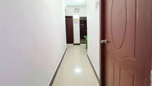 Un couloir avec une porte sur la droite, une chaise verte au loin et un panneau sur le mur.