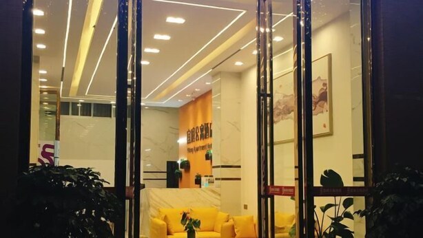 Un hall con un sofá amarillo, una pequeña mesa con una planta y un mostrador de recepción.