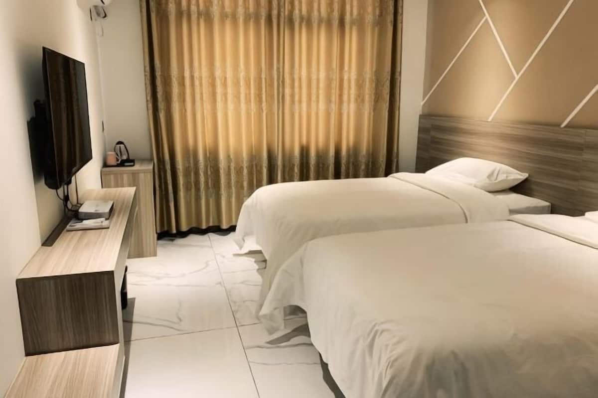 Una habitación de hotel con dos camas, televisión, mesita de noche y cortina.